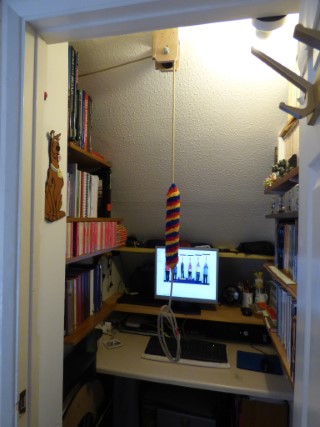 Front view of undestairs cupboards, with side shelving, laptop and bell rope hanging from ceiling.